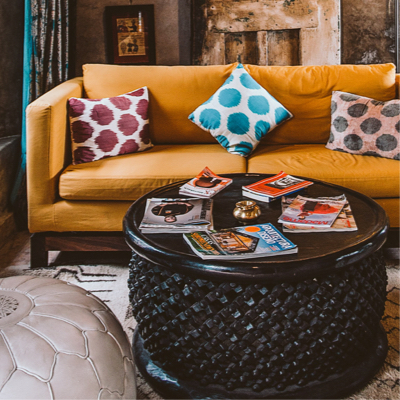 Room with orange sofa covered with three polka-dotted cushions, and circular wooden table topped with magazines.